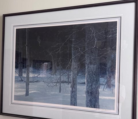 A framed Robert Bateman print of bare trees in snow, hanging on a wall.