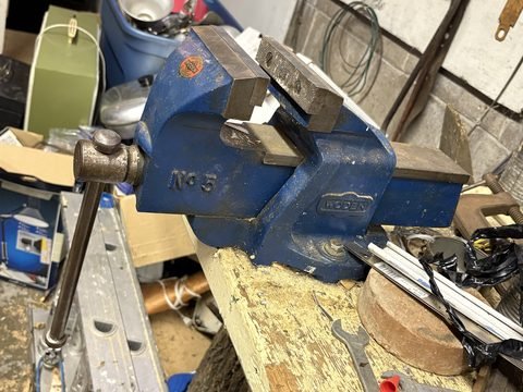 A blue Record No 5 bench vise clamped to a workbench in a full garage.